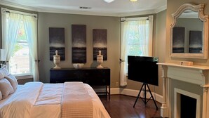 A bedroom with a large bed, a dresser, a TV on a stand, a fireplace, and a ceiling fan. - Charming & Spacious Historic Charlotte Home- in the heart of the city (Charlotte)