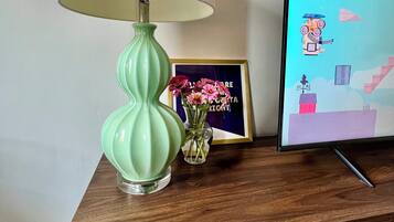 Ein Holzschrank mit einer grünen Lampe, einem gerahmten Bild und einer kleinen Vase mit Blumen.