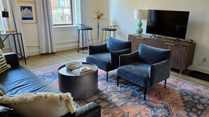 Ein Wohnzimmer mit einer Couch, zwei Sesseln, einem Couchtisch, einem Fernseher und einem gemusterten Teppich.