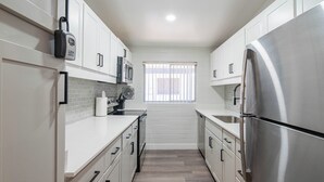 A modern kitchen with white cabinets, stainless steel appliances, and a window with blinds. - Dwell 7003-3 (Scottsdale)
