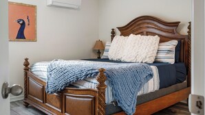 Ein Schlafzimmer mit einem hölzernen Bett, einer wandmontierten Klimaanlage und einem gerahmten Bild.