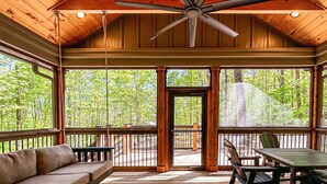 A covered outdoor area with a ceiling fan, a wooden deck, a sofa, and a table with chairs.