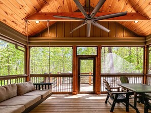 A covered outdoor area with a ceiling fan, a wooden deck, a sofa, and a table with chairs. - Hot Tub Cabin + Screened Porch | Red River Gorge (Beattyville)