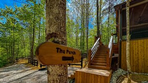 A wooden signpost with 'The Perch' written on it, a staircase leading to a wooden building, and a gravel path.