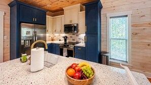 A kitchen with wooden ceiling, blue cabinets, stainless steel appliances, a granite countertop, and a fruit bowl.