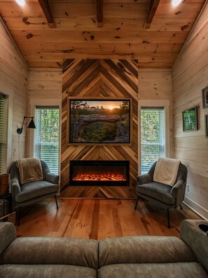 A cozy room with a fireplace, two armchairs, and a large framed picture above the fireplace. - Hot Tub Cabin + Screened Porch | Red River Gorge (Beattyville)