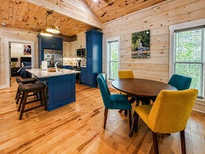 A wooden cabin interior with a kitchen, dining area, and a large window. - Hot Tub Cabin + Screened Porch | Red River Gorge (Beattyville)