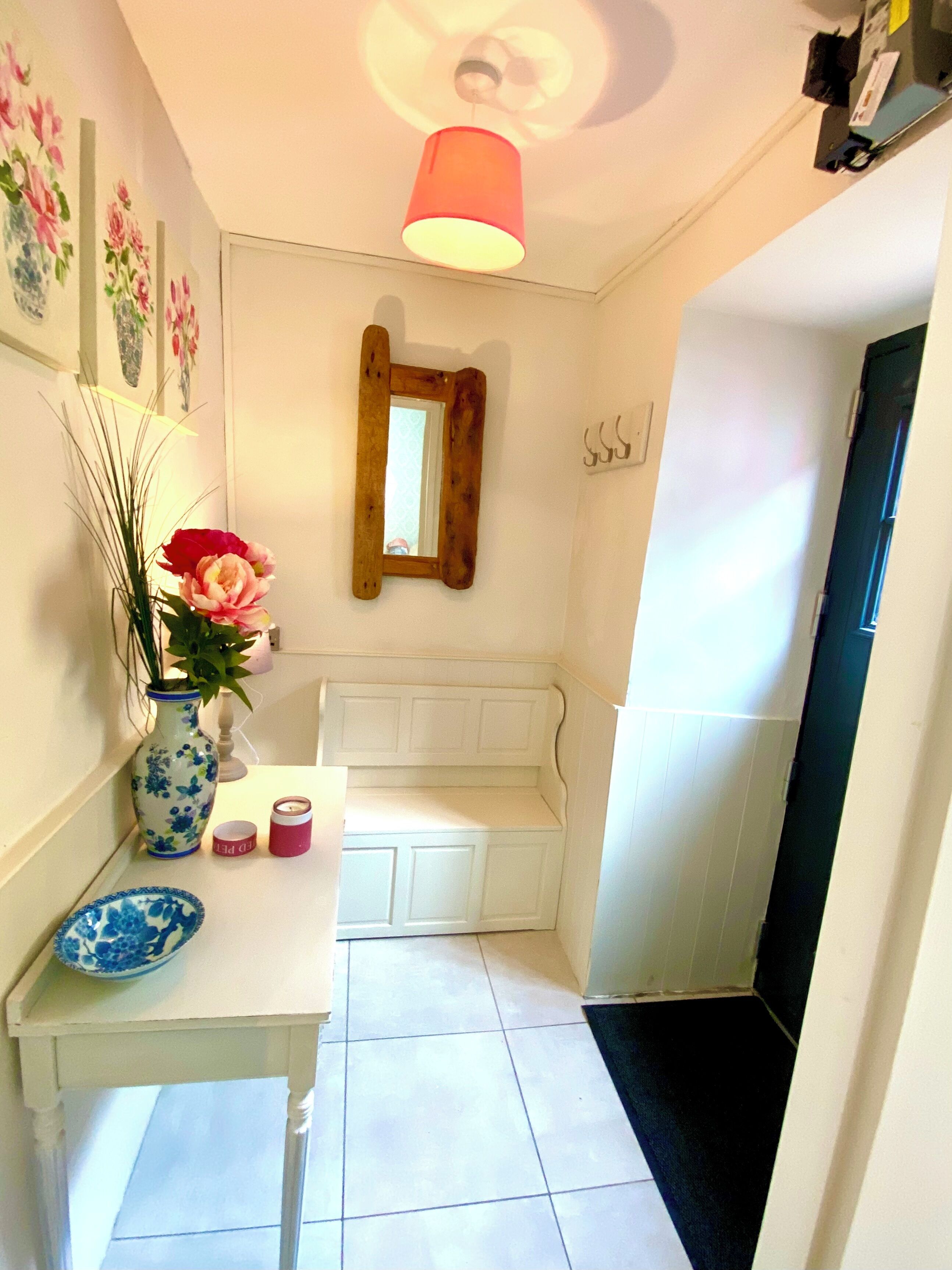 A hallway with a white bench, a vase with flowers, a mirror, and a ceiling light.