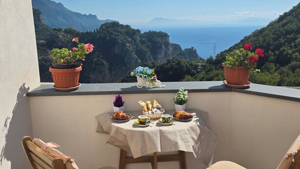 A balcony with a table set for breakfast, two chairs, and potted plants. - GREEN NEST with a sea view (Amalfi)