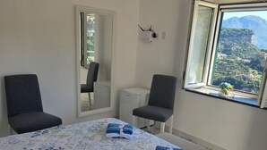 A hotel room with a bed, two chairs, a small table, a window with a mountain view, and a door. - GREEN NEST with a sea view (Amalfi)