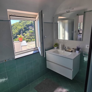 Ein Badezimmer mit großem Fenster, Waschbecken, Spiegel und einer Topfpflanze.