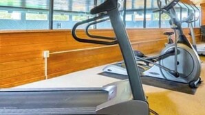 Un gimnasio con cintas de correr y bicicletas estáticas, paredes de madera y ventanas amplias.