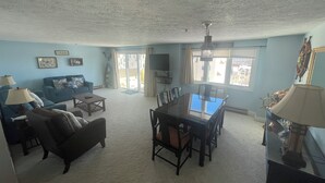 Una sala de estar con un sofá azul, una mesa de comedor con sillas y un ventanal con cortinas.