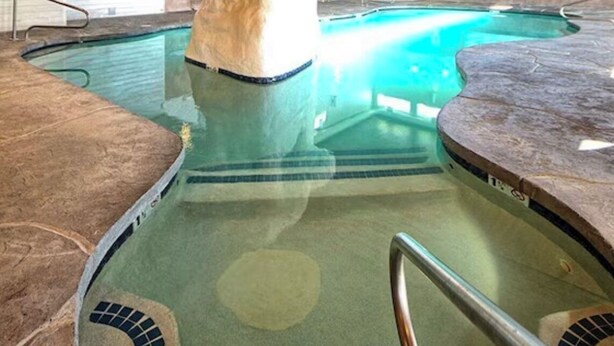 Una piscina interior con un pilar de piedra, suelo de baldosas y barandilla de metal.