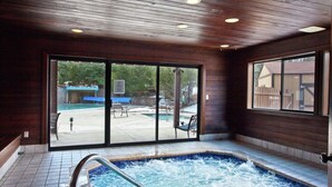 Ein Wellnessbereich mit Whirlpool, Holzwänden und Blick auf einen Hinterhof mit Schwimmbad und Terrassenmöbeln.