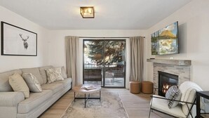 Ein Wohnzimmer mit einer Couch, einem Couchtisch, einem Kamin und einem großen Fenster mit Vorhängen.