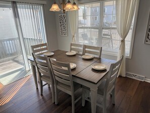A dining area with a wooden table and six chairs, a chandelier, and a window with blinds.