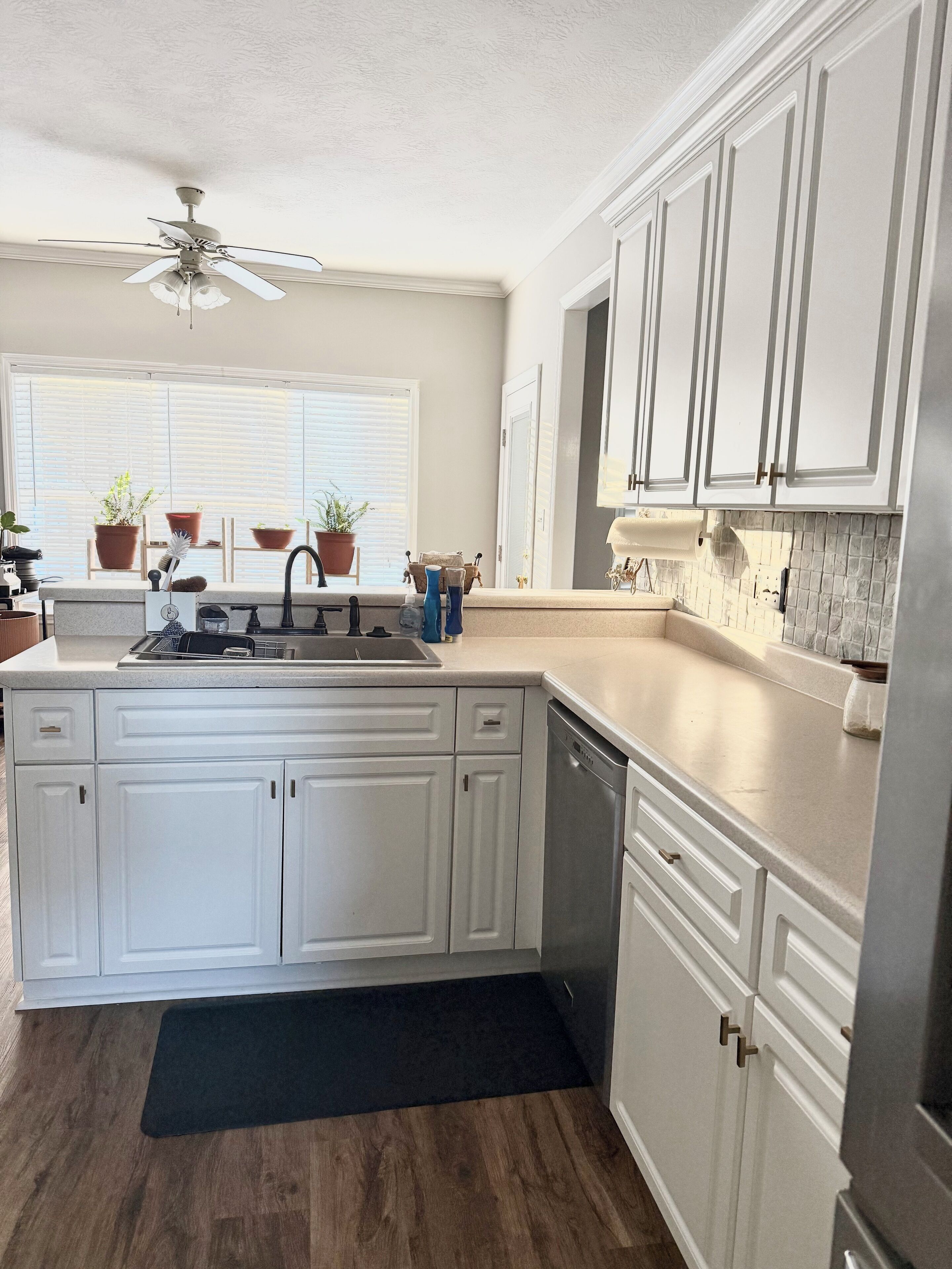 A kitchen with white cabinets, a dishwasher, a sink, and a ceiling fan.