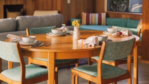 A wooden dining table with chairs, a sofa, and a window with a view of greenery. - Charming 2-bedroom house in Sea Ranch perfect for relaxing getaway (Sea Ranch)