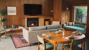 A living room with a fireplace, a television, a sofa, and a dining table set for four. - Charming 2-bedroom house in Sea Ranch perfect for relaxing getaway (Sea Ranch)