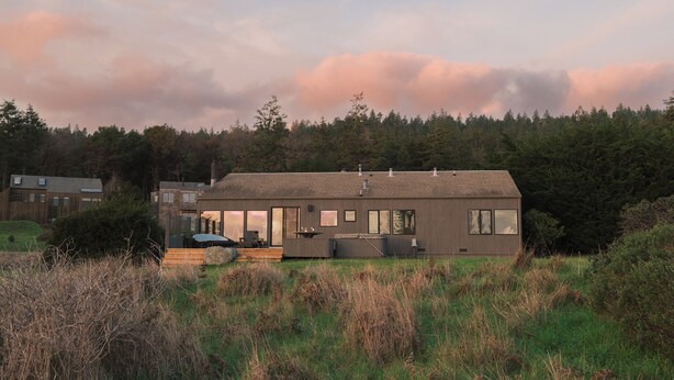 A modern house with a large garage, a covered outdoor seating area, and a view of a forested area. - Charming 2-bedroom house in Sea Ranch perfect for relaxing getaway (Sea Ranch)