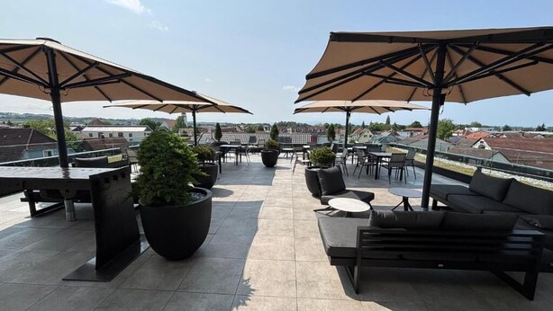 Una terraza en la azotea con mobiliario exterior, sombrillas y plantas en macetas.