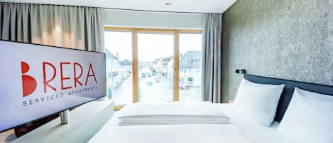 Una habitación de hotel con una cama grande, un televisor de pantalla plana y vistas a edificios a través de amplias ventanas.