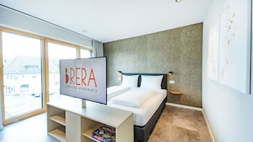 A modern bedroom with a large bed, a TV on a stand, and a window with a view of buildings outside.