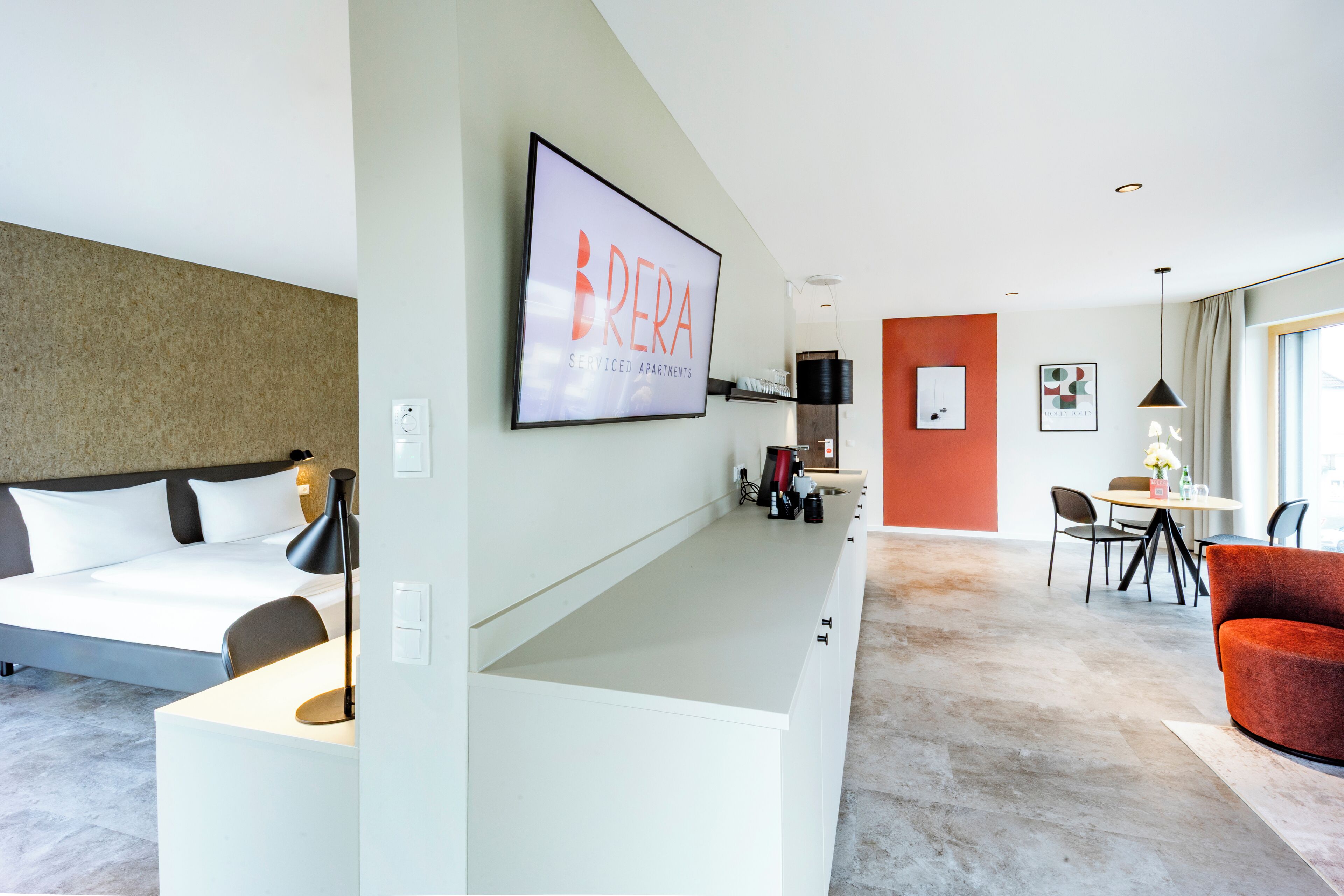 A modern hotel room with a bed, desk, and dining area.