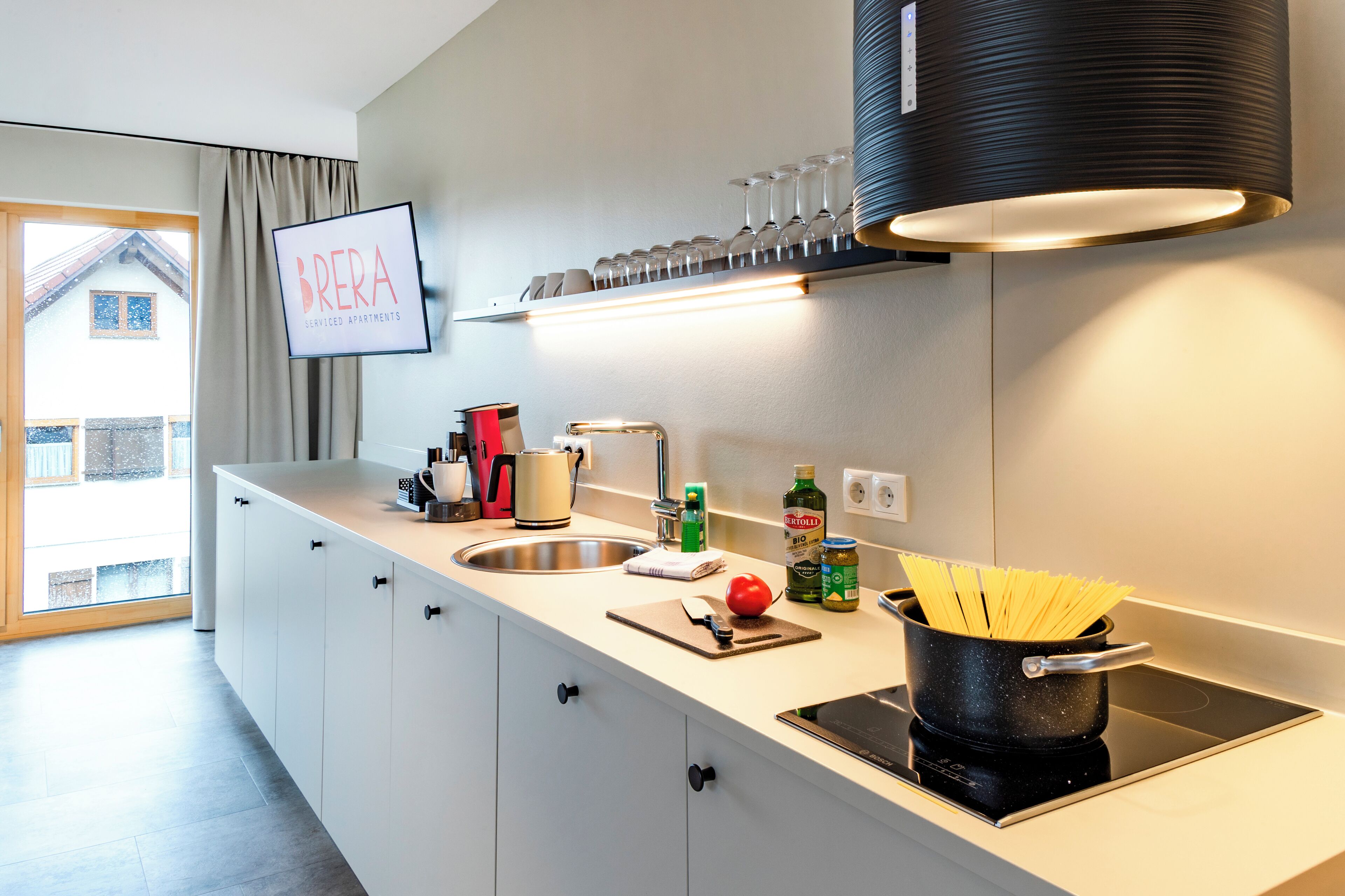 A modern kitchen with a built-in stove, a sink, and a countertop with various kitchen items.