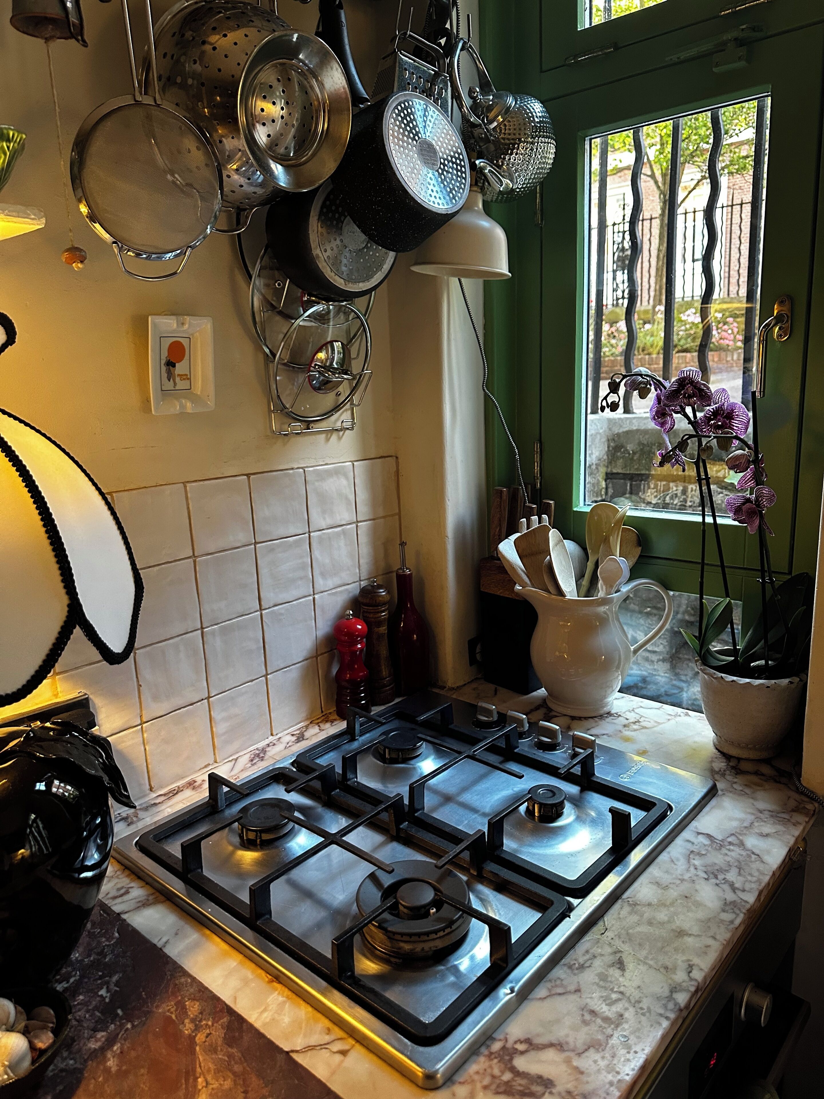 A kitchen with a gas stove, hanging pots, and a window with a view of the outside.