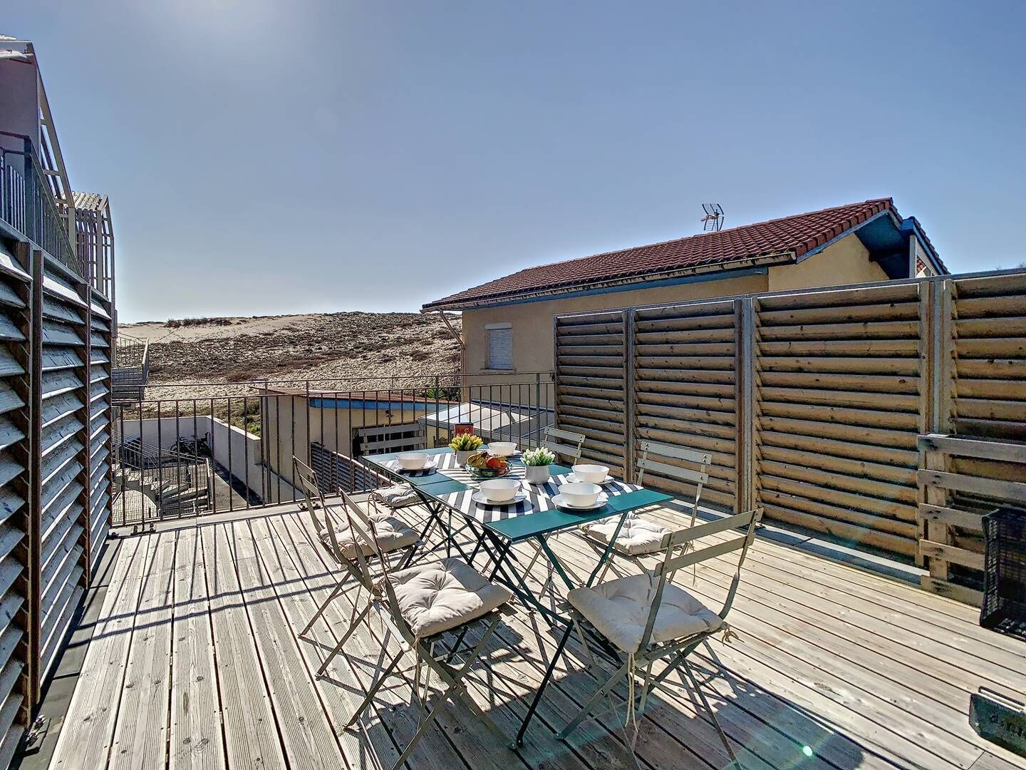Een houten terras met een eettafel, omringd door stoelen.