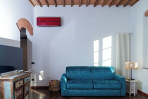 A living room with a blue sofa, a wooden cabinet, a red air conditioner, and a window with vertical blinds. - Under The Tower Pisa (Pisa)