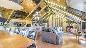 Een moderne loft met hoge plafonds, zichtbare balken, een keukenhoek en een zithoek met een bank en stoelen.
