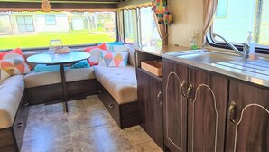 Een compacte kitchenette met een spoelbak, een klein tafeltje en een zithoek met kussens.