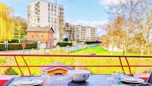 A dining area with a view of a modern apartment building, a small red house, and a fenced green space. - Duplex 6 persons with 2 parking spaces - Honfleur (Honfleur)