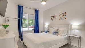 A modern hotel room with a large bed, a bedside table, a nightstand, a window with curtains, and artwork on the wall. - Las Olas Chic Apt w/ Patio & Free Parking (Fort Lauderdale)