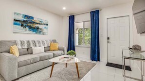 A modern living room with a grey sofa, a white coffee table, and a painting on the wall. - Las Olas Chic Apt w/ Patio & Free Parking (Fort Lauderdale)