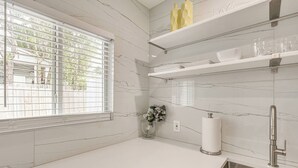 A kitchen with a marble backsplash, a window with blinds, a vase with flowers, and a stainless steel sink. - Las Olas Chic Apt w/ Patio & Free Parking (Fort Lauderdale)
