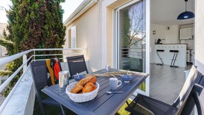 A balcony with a table set for breakfast, including bread, a thermos, and cups.