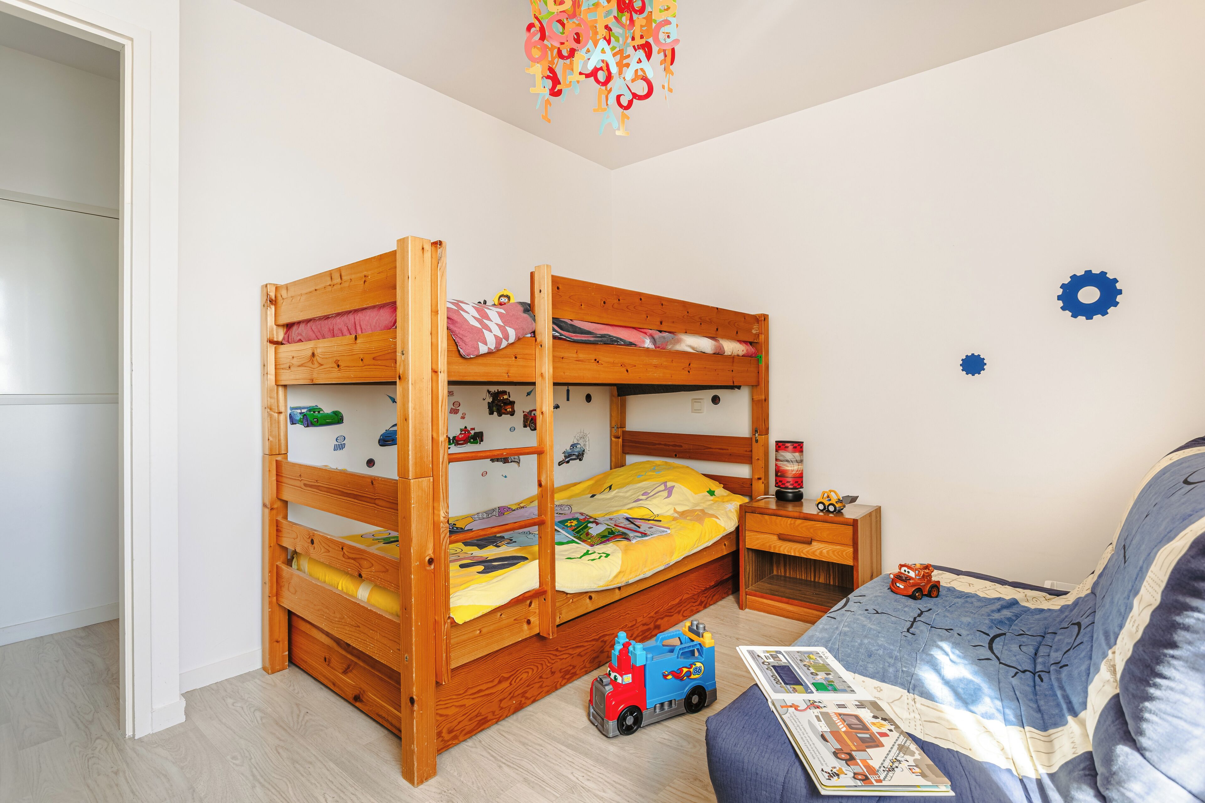 A bunk bed with a desk and chair, toys, and a bedspread with a car design.