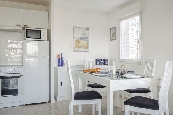 A modern kitchen with white cabinetry, a microwave, an oven, and a dining table set for four with chairs. - Apartment in a secure complex, near La Rochelle, Châtelaillon-Plage (Aytré)