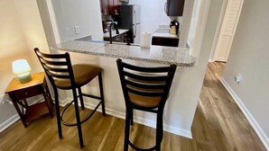 A compact kitchen with dark wooden cabinets, a granite countertop, and two bar stools.