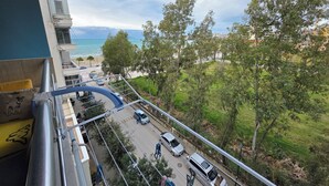 A balcony with a view of a beach, parked cars, and greenery. - Bes' Marina Studio (Vlore)