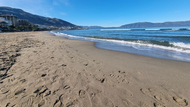 A beach with footprints in the sand, a clear blue sky, and mountains in the background. - Bes' Marina Studio (Vlore)