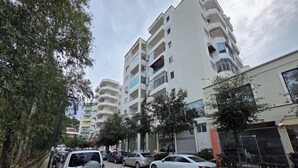 A multi-story residential building with balconies, parked cars, and trees along the sidewalk. - Bes' Marina Studio (Vlore)