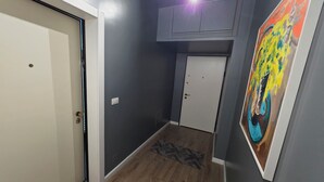 A hallway with a wooden floor, a white door, a gray wall, and a colorful painting. - Bes' Marina Studio (Vlore)