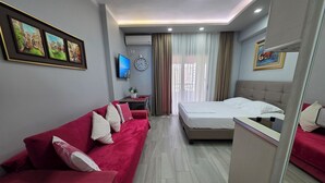 A modern hotel room with a red sofa, a bed, a desk, and a TV. - Bes' Marina Studio (Vlore)