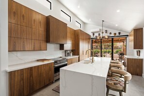 Une cuisine moderne avec des meubles en bois, un plan de travail en marbre et un îlot central doté de tabourets de bar.