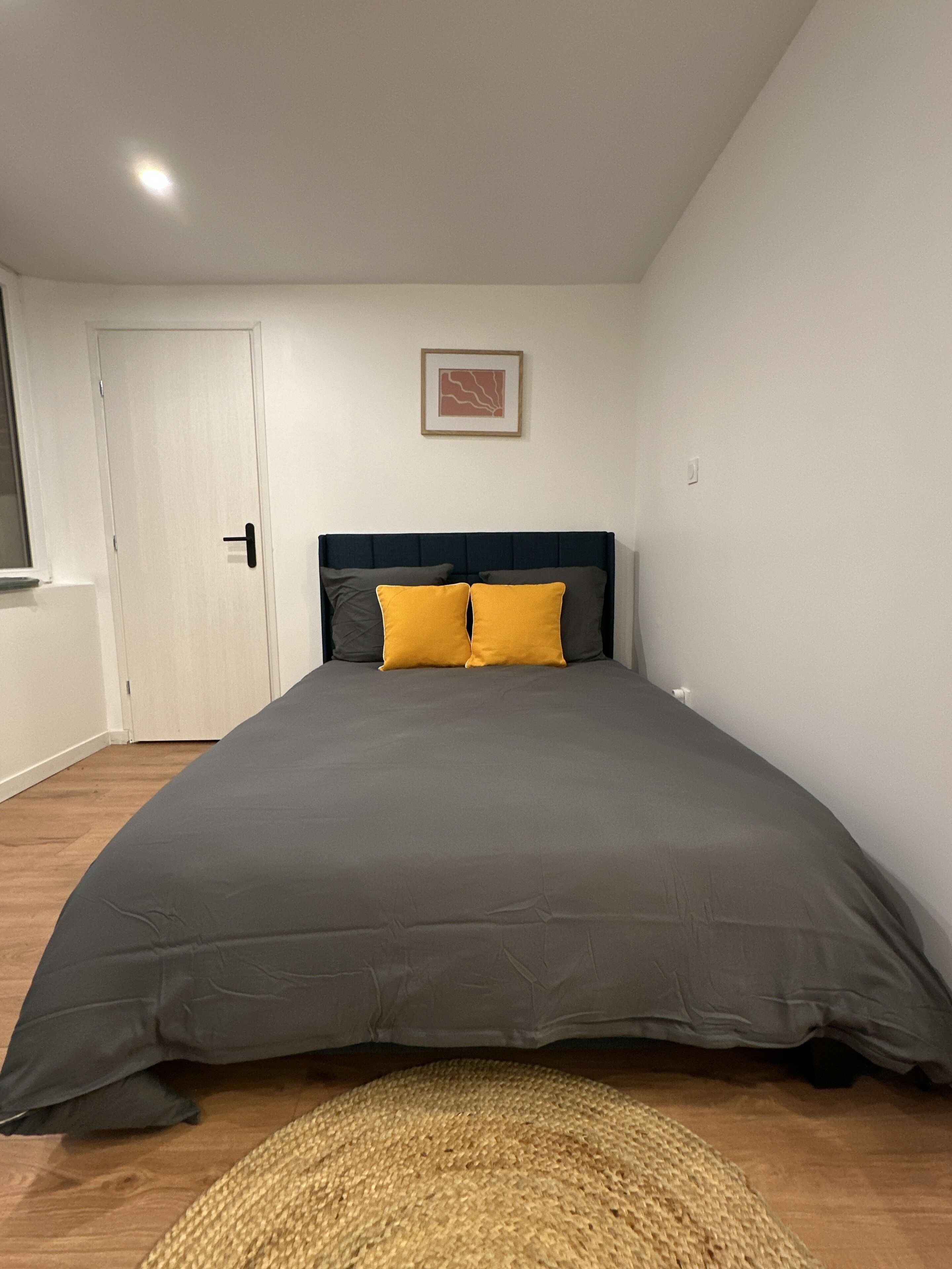 A bedroom with a large bed, a door, a window, and a framed picture on the wall.
